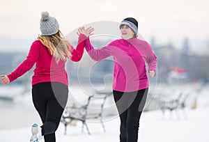 Mother and daughter wearing sportswear and running on snow during winter