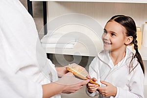 mother and daughter in white bathrobes holding hairbrush