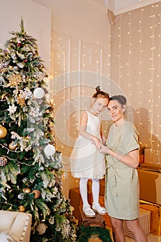 mother and daughter in a white dress at the Christmas tree.