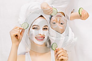 Mother and daughter in white shirts and white towels on their heads in a home bathroom, doing spa procedures with mud