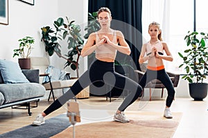 Mother and daughter working out at home, doing leg stretches, side to side lunges