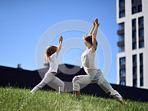 Mother and daughter working out practicing yoga outside on a grass together urban city  park