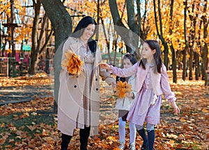 Mother and daughters are in autumn city park, happy people walking together, family with children, playing with yellow leaves,