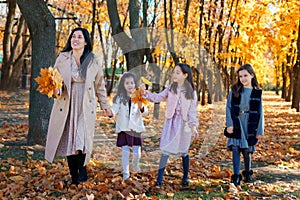 mother and daughters are in autumn city park, happy people walking together, family with children, playing with yellow leaves,