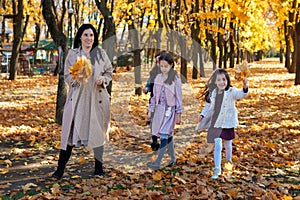 mother and daughters are in autumn city park, happy people walking together, family with children, playing with yellow leaves,