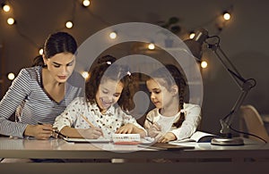 Mother with daughters drawing on paper doing homework at home in evening