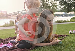 Mother with daughters having picnic by river, she chats on smartphone