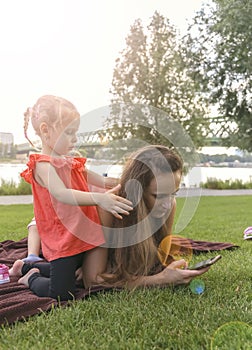 Mother with daughters having picnic by river, she chats on smartphone