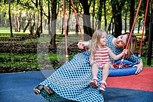 Mother and daughters on a swing in the park among the trees. Concept mom daughter, family happiness, relaxation in the