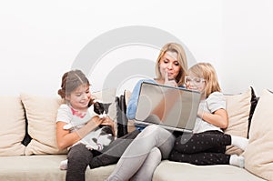 Mother and daughters using laptop and playing with the cat