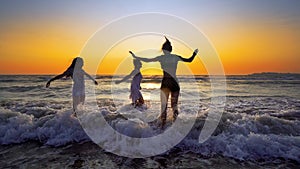 Mother and daughters walking, jump and playing on the beach at sunset