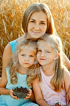 Mother and daughters in a wheat field. A happy family in the fresh air on a picnic outside the city on a sunny summer day
