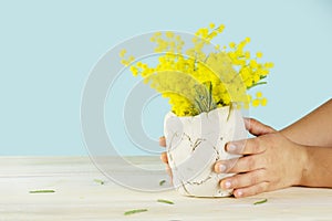 Mother day gift. Child`s hands holding a diy ceramics vase with yellow flowers. Isolated on blue background