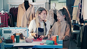 Mother designer and a little girl are cutting fabric together