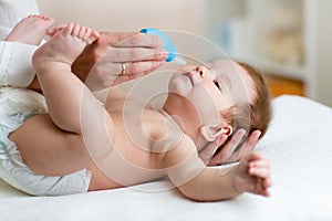 Mother or doctor cleans baby`s nose with blower, while infant is lying and smiling.