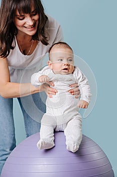 Mother does useful exercises by her infant son, on fitness ball