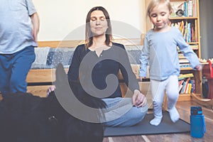 Mother doing yoga, calm and relaxed while kids and dog run around making noise