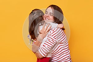 Mother and doughter hug each other with love, little cute girl wishes joy her mom on holiday, pose  over yellow studio