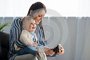 mother dressing cheerful little baby on sofa