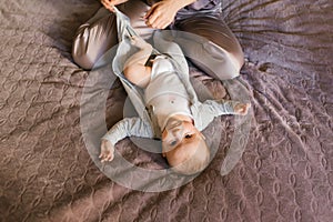 Mother dressing her newborn baby son lying on bed