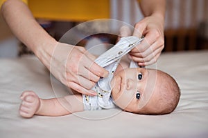 Mother dressing her newborn baby son lying on bed