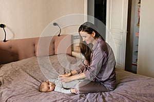 Mother dressing her newborn baby son lying on bed
