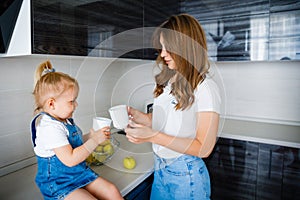 Mother is drinking tea in the kitchen with her little daughter.