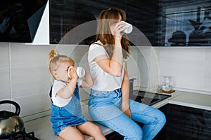 Mother is drinking tea in the kitchen with her little daughter.