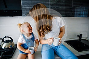 Mother is drinking tea in the kitchen with her little daughter.