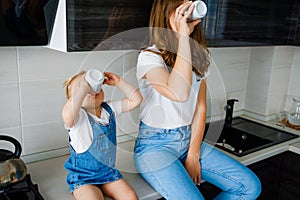 Mother is drinking tea in the kitchen with her little daughter.