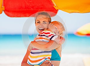 Mother embracing baby on beach under umbrella