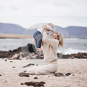 Mother enjoying winter vacations holding, playing and lifting his infant baby boy son high in the air on sandy beach on