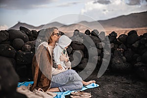 Mother enjoying winter vacations playing with his infant baby boy son on black sandy volcanic beach of Janubio on