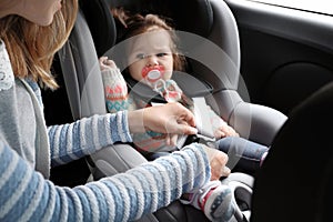 Mother fastening baby to child safety seat car