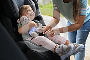 Mother fastening her daughter in child safety seat inside car