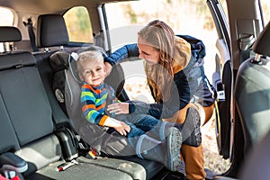 Mother fastening safety belt for her baby boy in his car seat