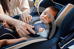 mother is fastening safety belt to newborn baby in car seat