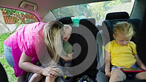 A mother fastens her son's seat belt in the back seat of the car.