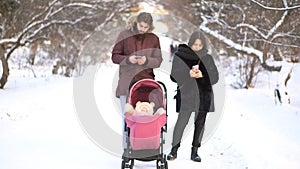 Mother and father addicted to mobile phones neglecting baby in stroller and while walking in winter park. Parents busy