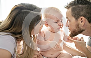 Mother father and baby child on a white bed.