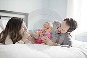 Mother father and baby child on a white bed.