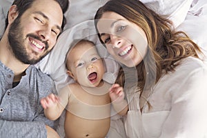 Mother father and baby child on a white bed.