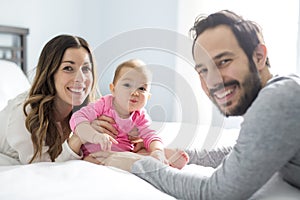 Mother father and baby child on a white bed.