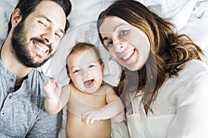 Mother father and baby child on a white bed.