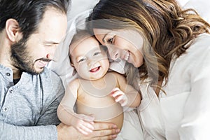 Mother father and baby child on a white bed.