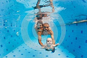 Mother, father with baby swimming, diving underwater in pool