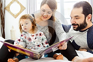 A mother father and child daughter reading book in bed before going to sleep