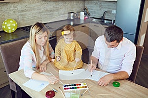 Mother, father and child draw together at the table.