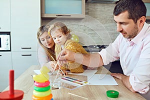 Mother, father and child draw together at the table.