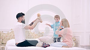 Mother father and child son play in bed. Young family being playful at home. Happy parents playing with their son on the